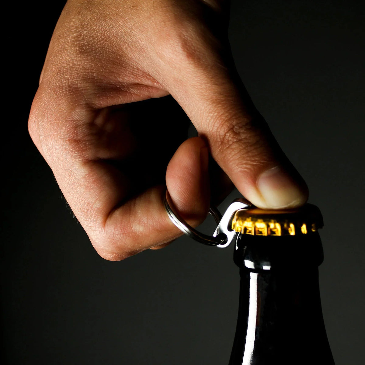 Hand using compact keychain bottle opener on capped glass bottle, Gear Carry accessory