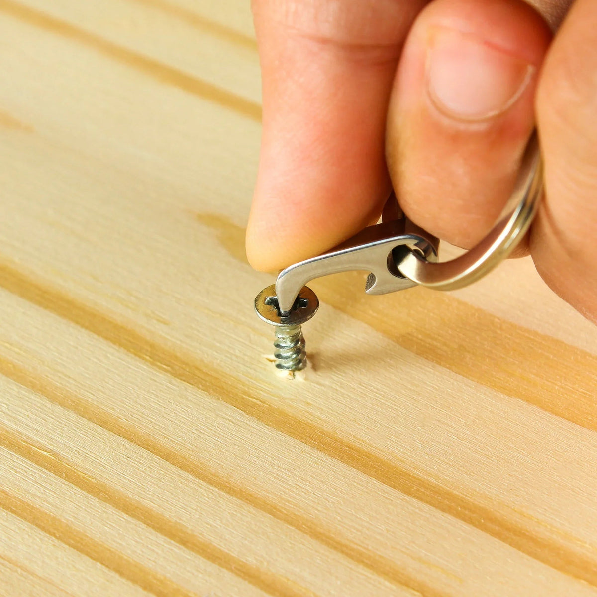 Compact metal keychain tool unscrewing a screw on light wood surface, Gear Carry accessory