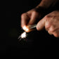 Hands striking a fire starter tool, creating sparks on black background, Gear Carry accessory