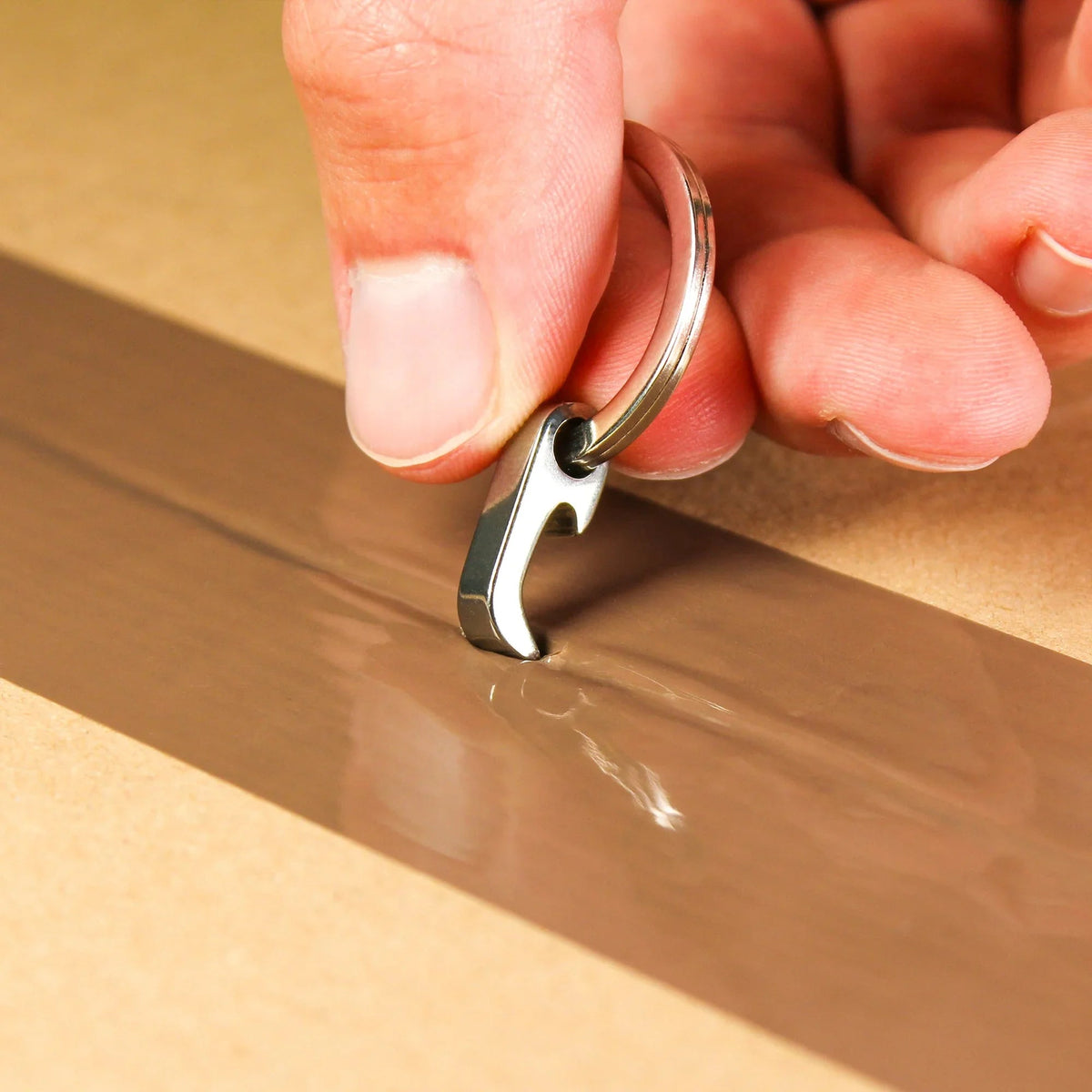 Hand using compact Gear Carry keychain tool to open taped cardboard box