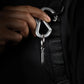 Hand holding silver carabiner clip with compact metal keychain on black backpack strap