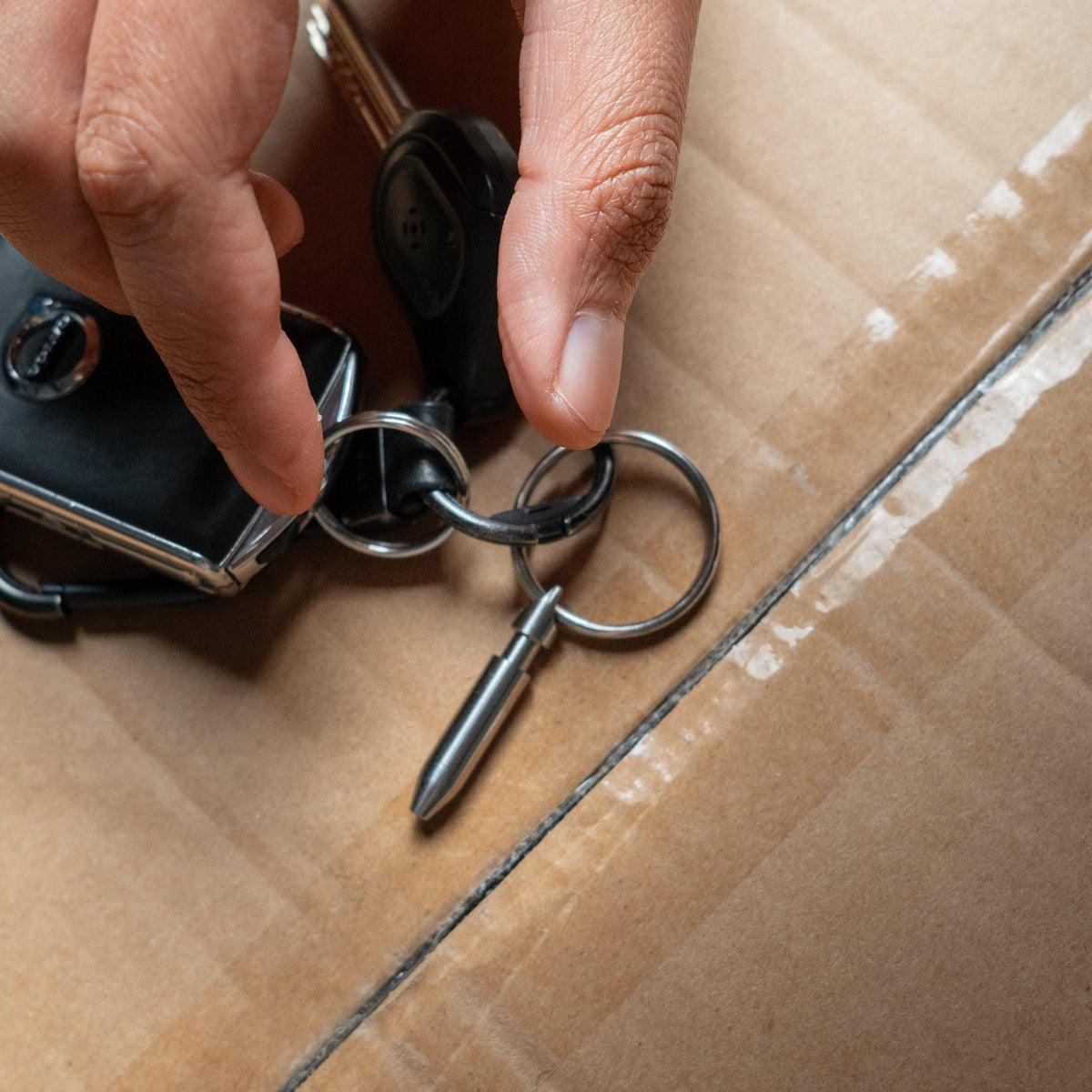 Hand holding compact metal keychain tool and keys on cardboard, Gear Carry everyday carry