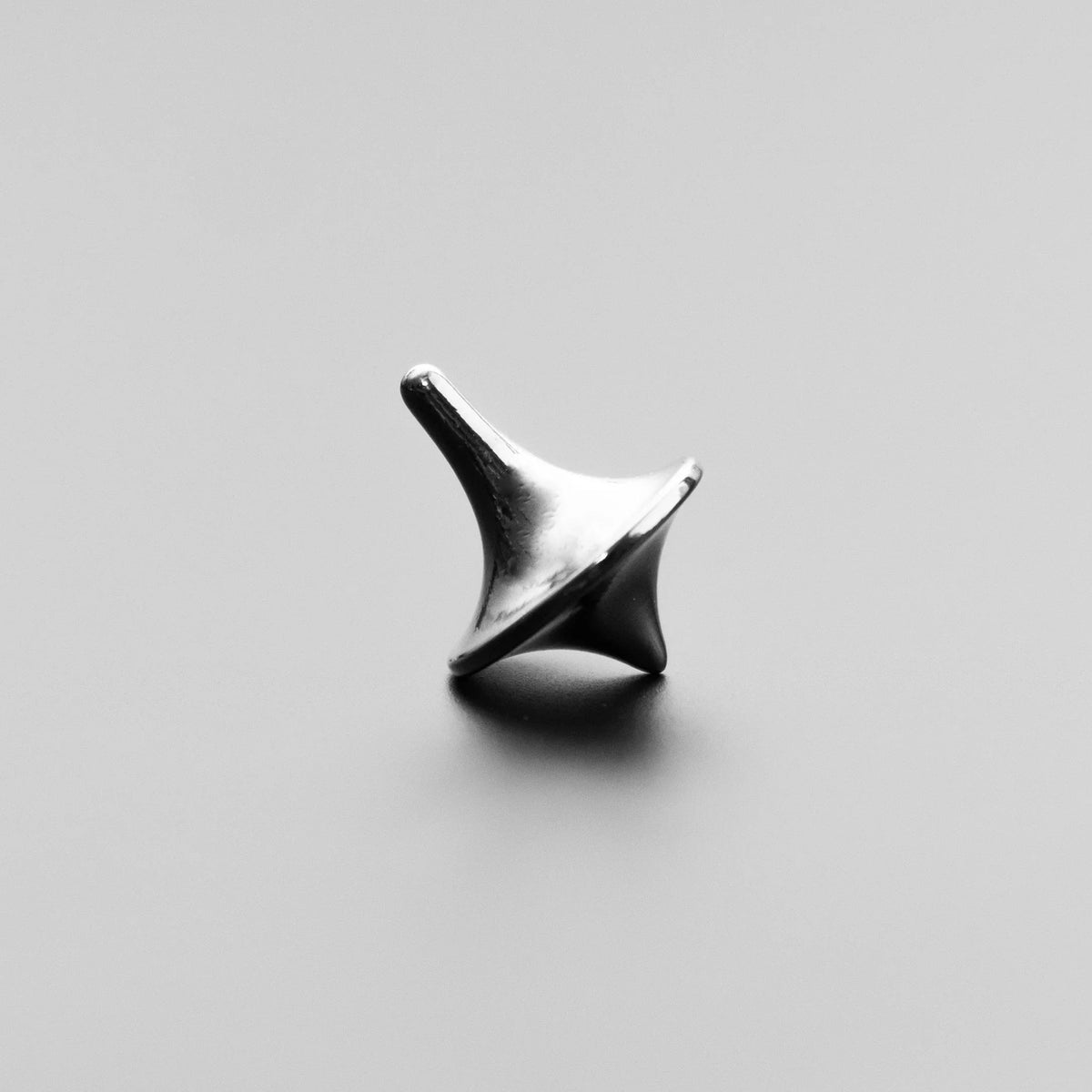 Minimalist metal spinning top on smooth grey surface, small durable carry accessory