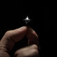 Hand holding a compact metal spinning top from Gear Carry against a dark background.