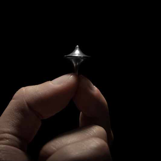 Hand holding a compact metal spinning top from Gear Carry against a dark background.
