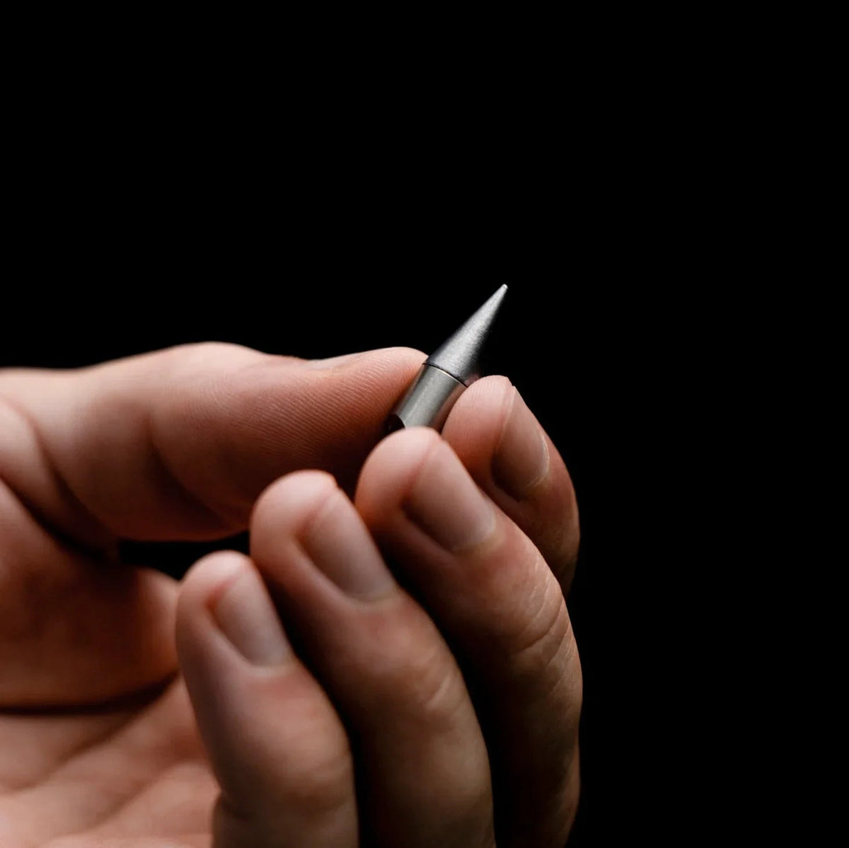 Hand holding a compact metal everyday carry tool against a black background
