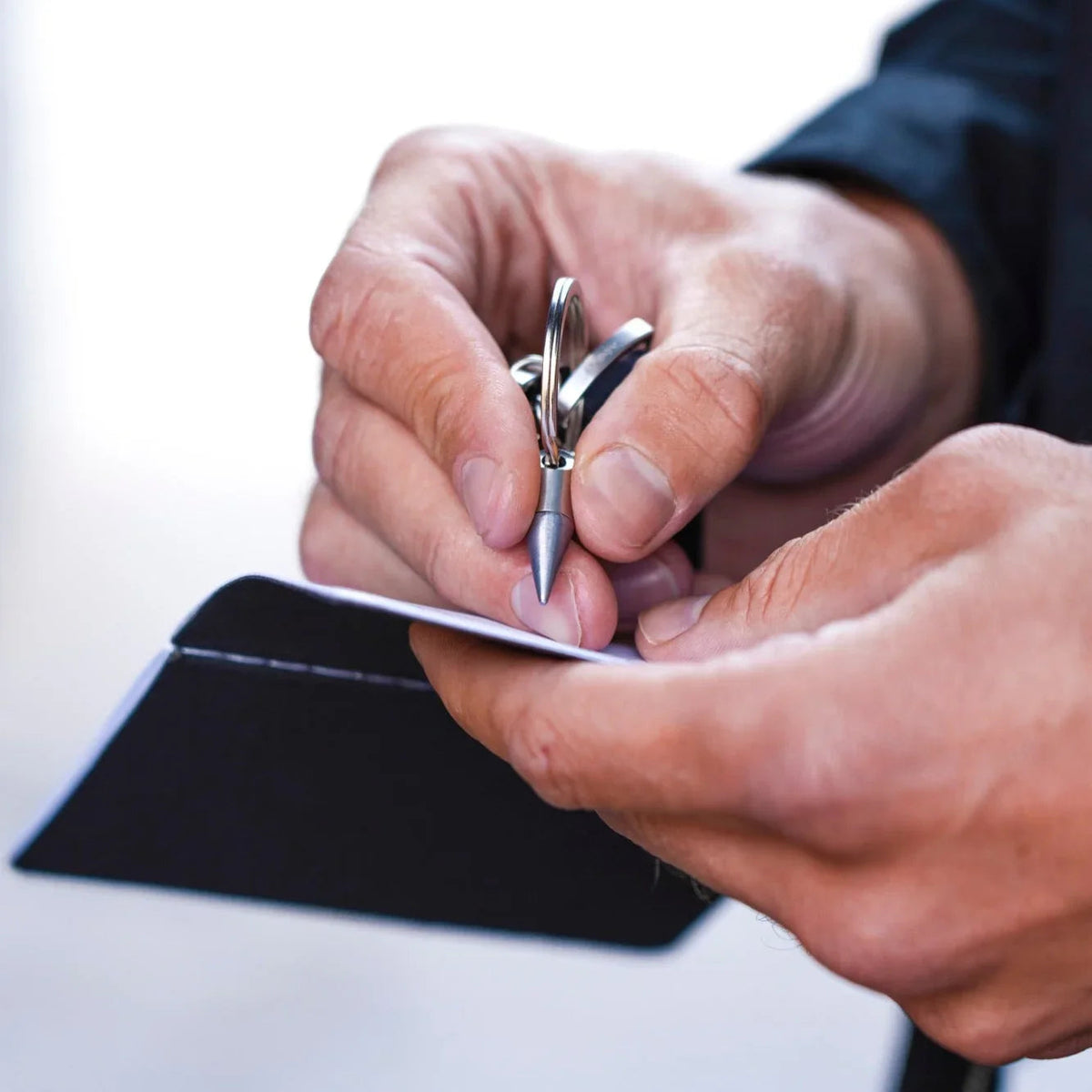 Man writing with compact keychain pen on notepad, everyday carry accessory by Gear Carry