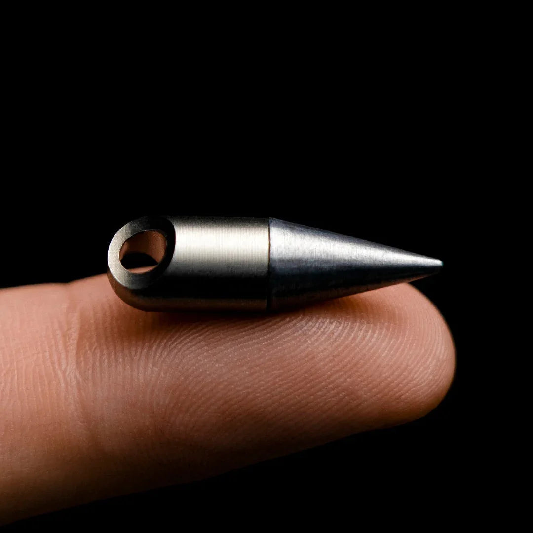 Compact metal everyday carry keychain tool resting on a fingertip, black background
