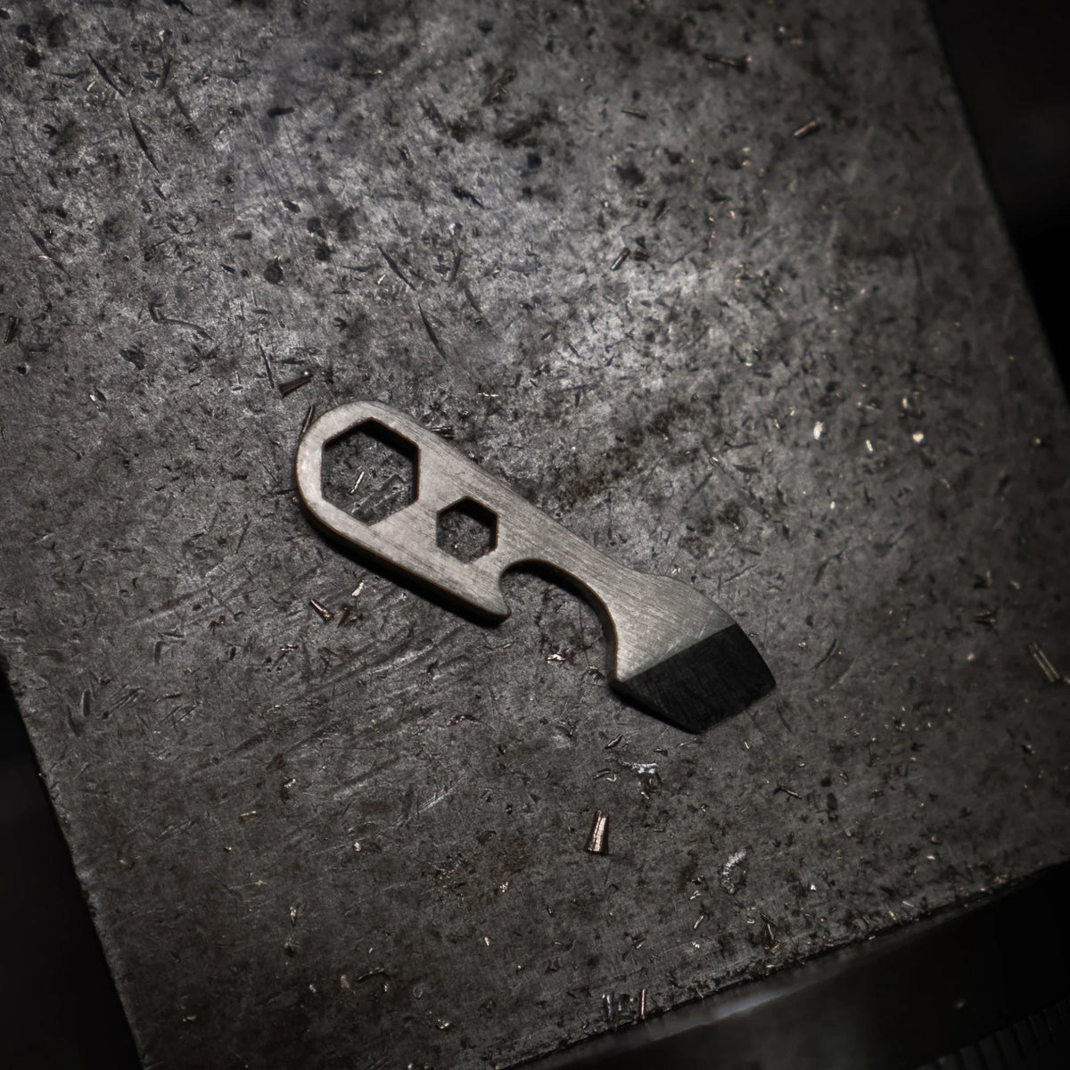 Compact metal multi-tool with hex and pry features on a dark textured surface, Gear Carry accessory
