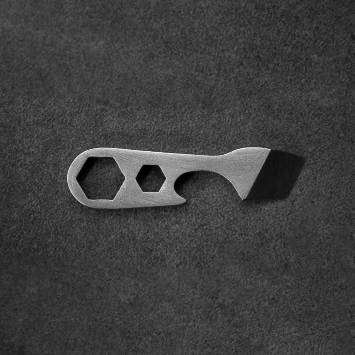 Compact metal multi-tool with hex wrenches and pry bar on dark textured background