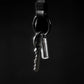 Minimalist keychain with silver key and metal capsule on black background, Gear Carry accessory