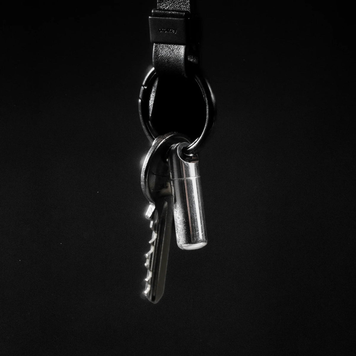 Minimalist keychain with silver key and metal capsule on black background, Gear Carry accessory