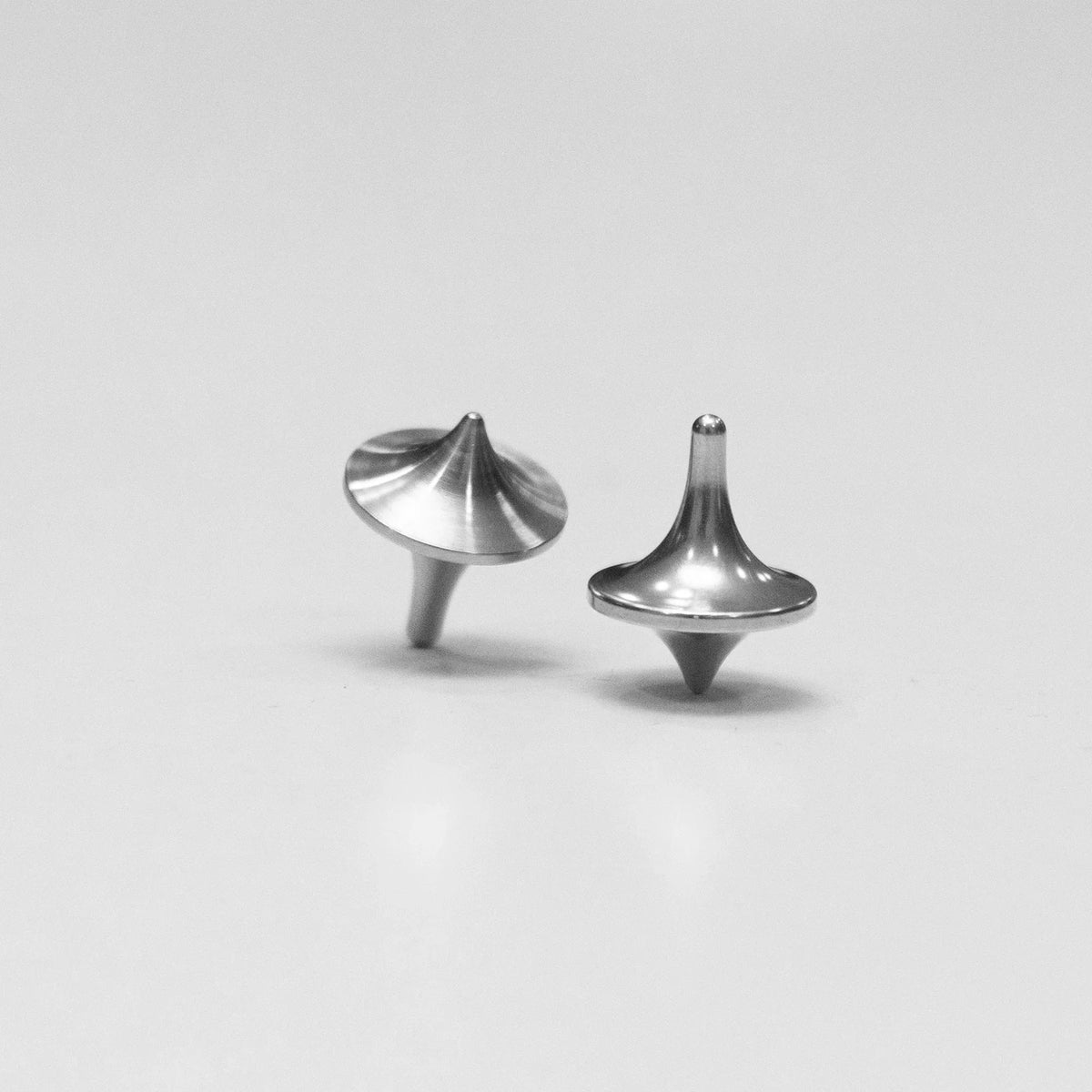 Two compact metal spinning tops on a plain surface, durable everyday carry accessory.