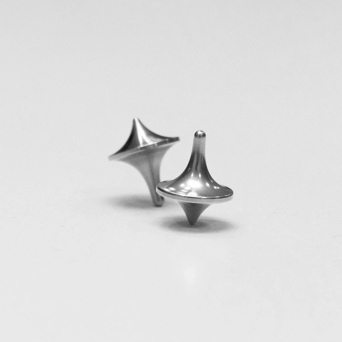 Two metal spinning tops on a plain surface, compact everyday carry accessory by Gear Carry